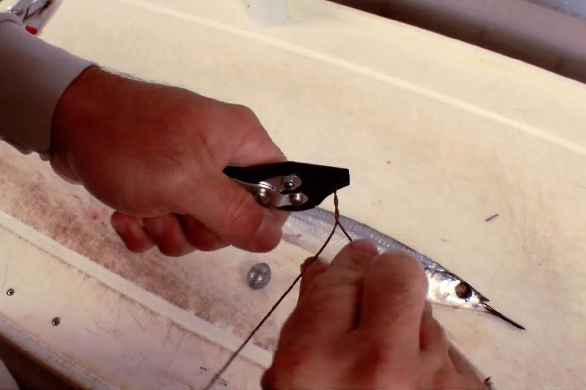 Angler's hands tying a haywire twist on single-strand stainless wire to secure a wahoo leader connection to a fishing hook.